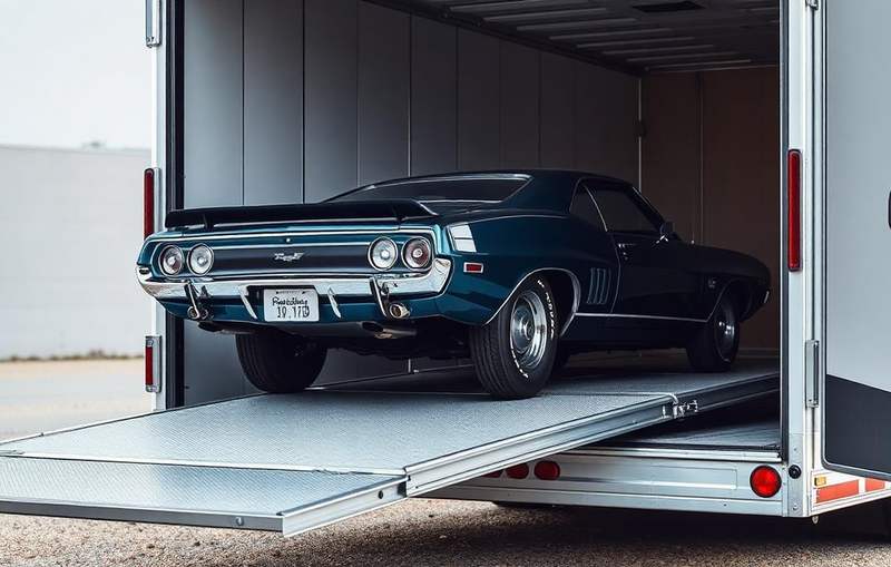 Classic muscle car being rolled into an enclosed transport trailer